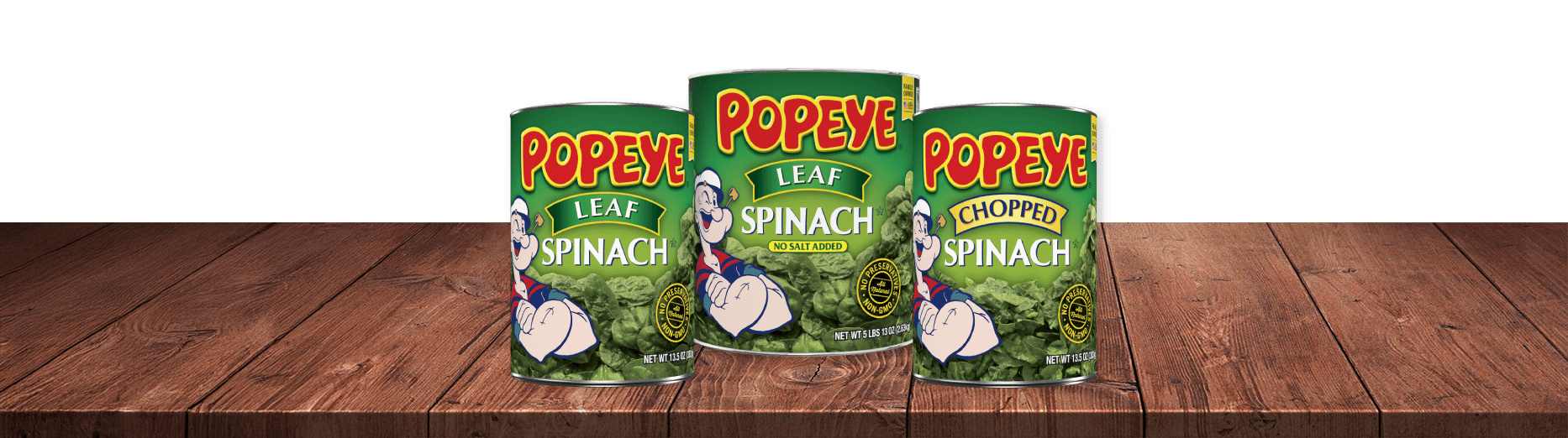 3 cans of Popeye Spinach on a Wood Table